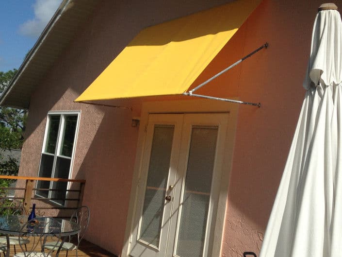 Exterior of a pink house featuring a yellow awning above glass doors and a patio table.