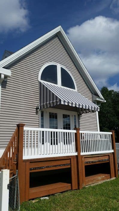 Modern house with a unique arched window and striped awning over a wooden deck.
