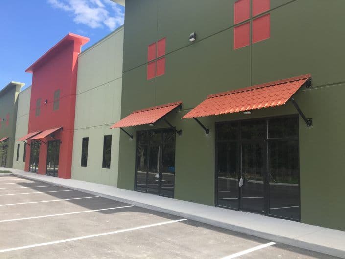 Colorful commercial building exterior with red and green walls and red awnings over glass doors.