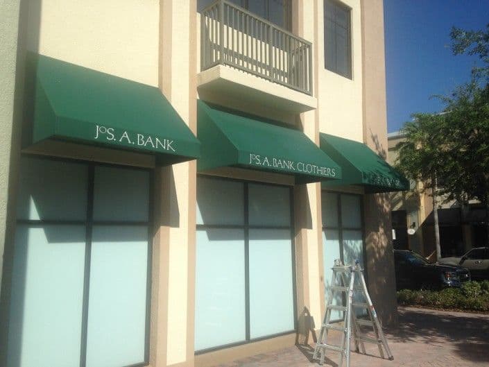 Green awnings of Jos. A. Bank Clothiers on a retail building with a ladder nearby.