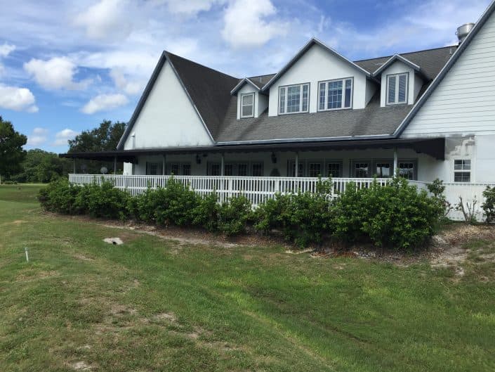 White house with a sloped roof and porch surrounded by greenery and blue sky.