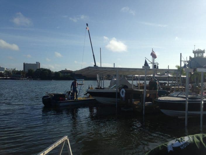 Boats docked at a marina with a crane and American flag under a clear blue sky.