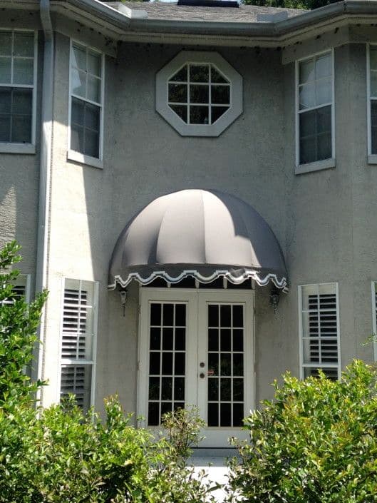 Exterior of a house featuring a gray awning over double doors and decorative windows.