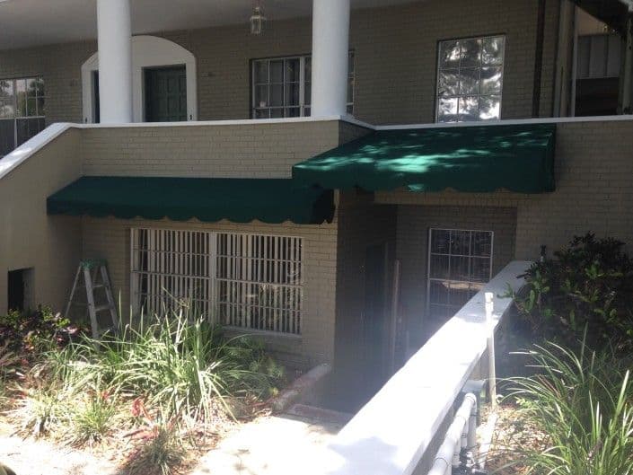 Green awnings over an apartment entrance with landscaping and a ladder nearby.
