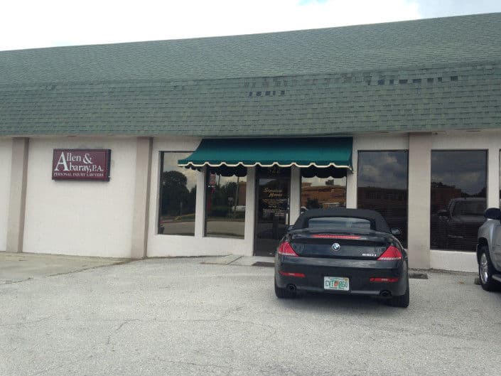 Office building of Allen & Barry, P.A. with green awning and parked black car outside.