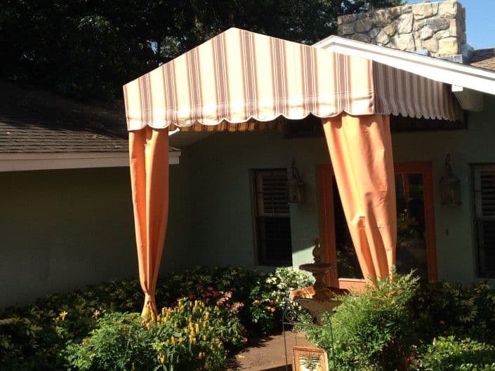 Striped awning over entrance surrounded by colorful flowers and greenery.