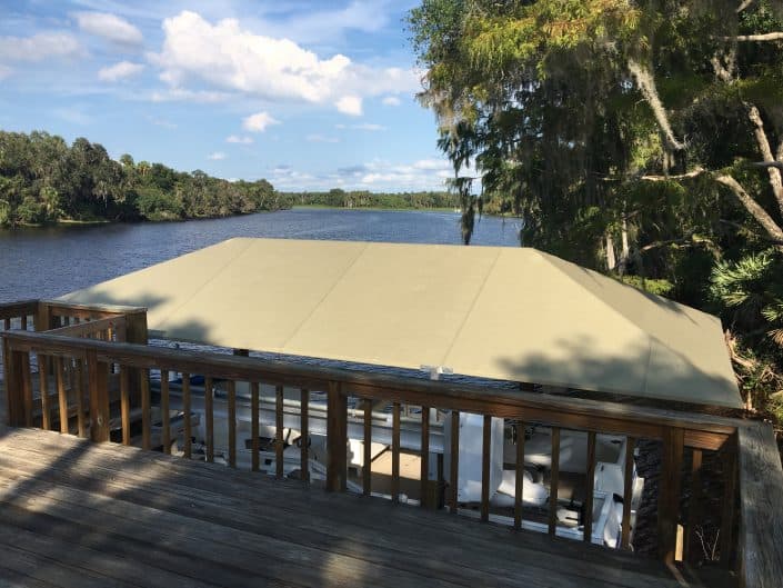 View of a boat dock covered with a tan tarp beside a peaceful river under blue skies.