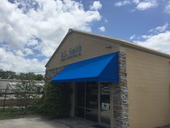 B.L. Smith Building Contractors storefront with blue awning and stone accents under a cloudy sky